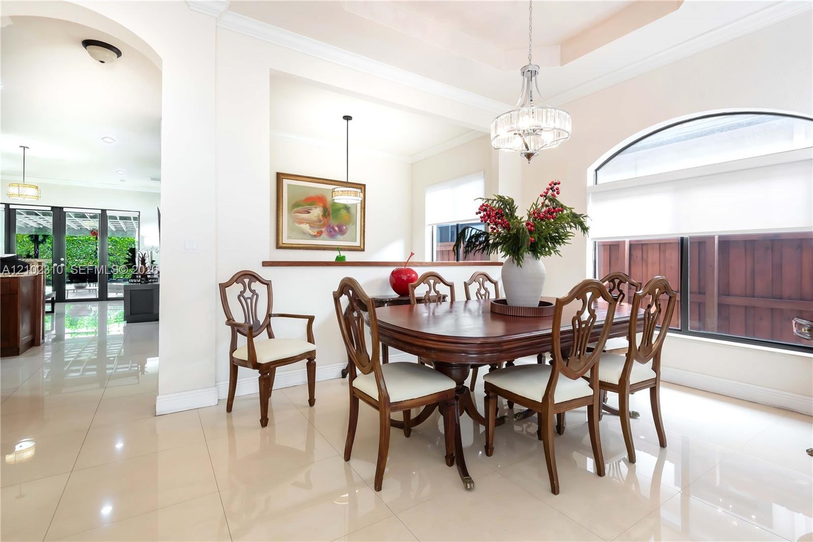 Dining area featuring polished tile flooring, a recessed tray ceiling, a multi-tiered crystal chandelier, and a large arched window