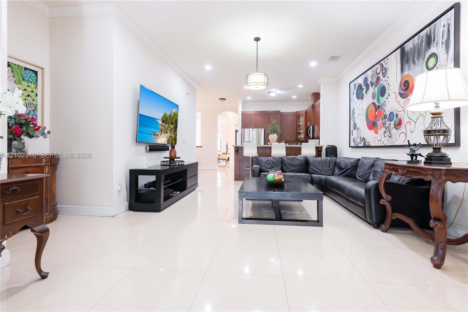 Polished large-format tile flooring, recessed ceiling lighting, crown molding, and an open kitchen featuring a tiered breakfast bar