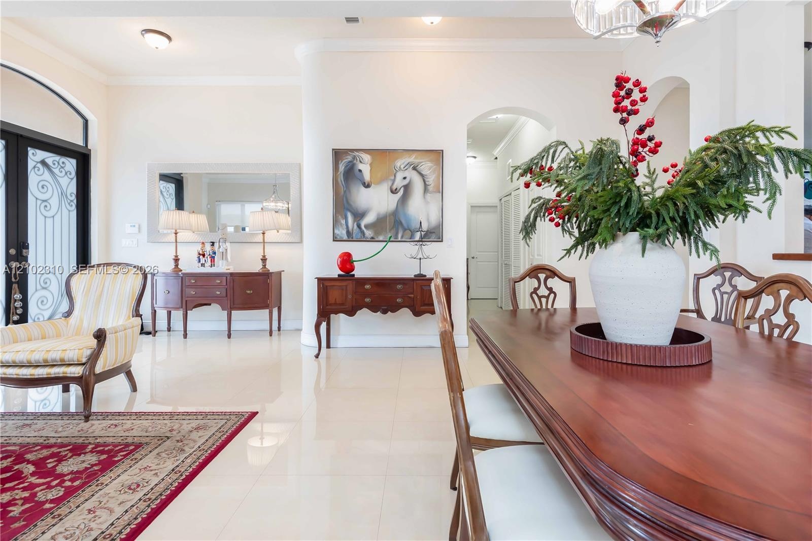Open-concept interior featuring polished tile flooring, arched doorways, curved architectural wall accents, recessed lighting, and a tiered chandelier
