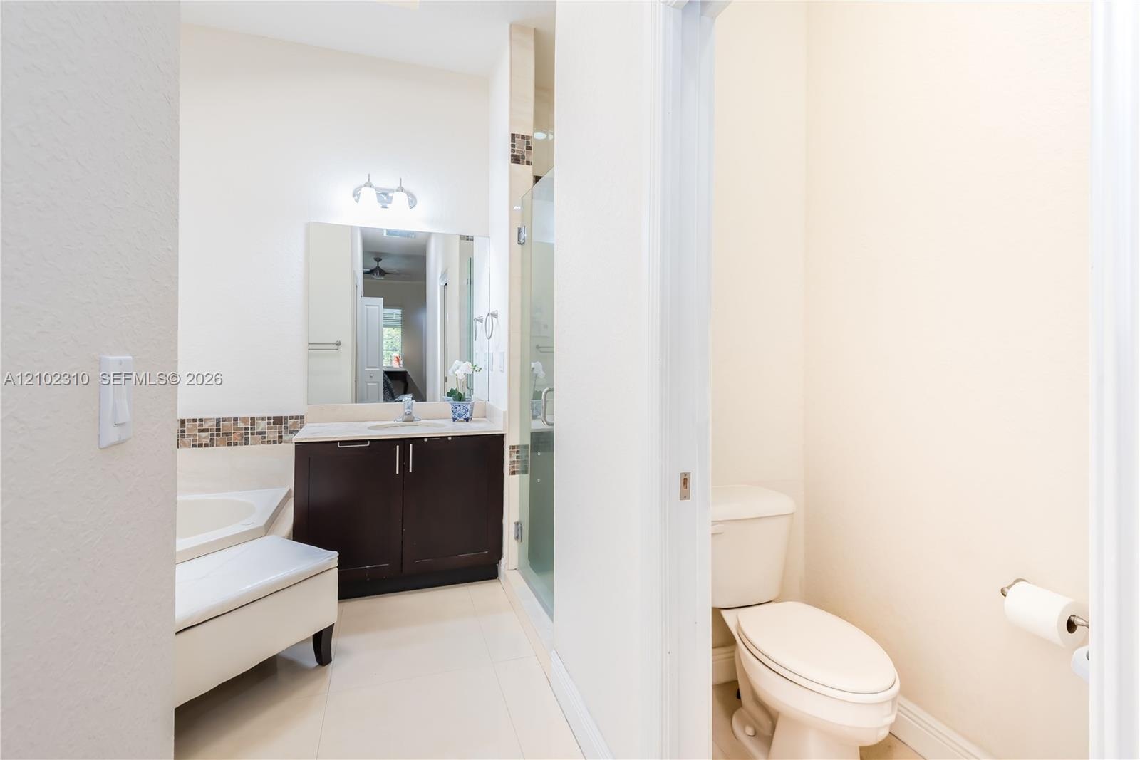Dark wood cabinetry, solid surface countertop, glass-enclosed shower, soaking tub, and tile flooring