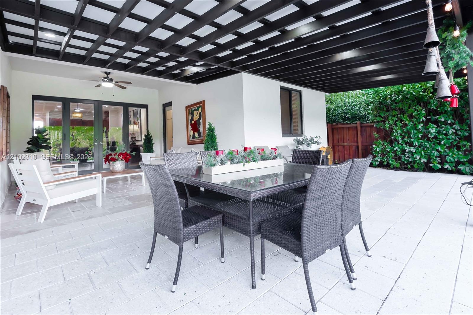 Covered patio featuring a dark-finish pergola, light-toned stone tile flooring, integrated ceiling fan, and glass French doors