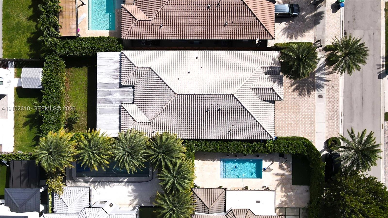 Aerial perspective of the property featuring a tile roof, paved driveway, swimming pool, and landscaped perimeter hedging