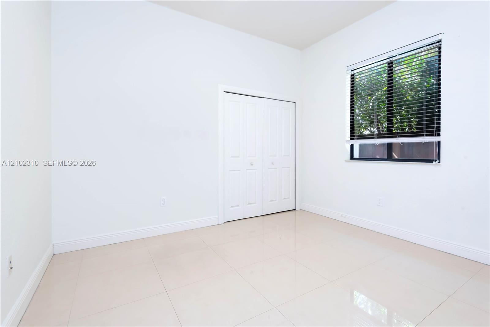 Neutral-toned ceramic tile flooring, dual-panel closet doors, and window featuring horizontal blinds
