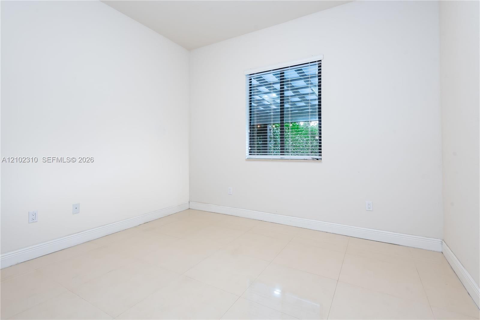 Neutral interior room featuring large-format tile flooring, crisp white walls, and a window fitted with horizontal blinds