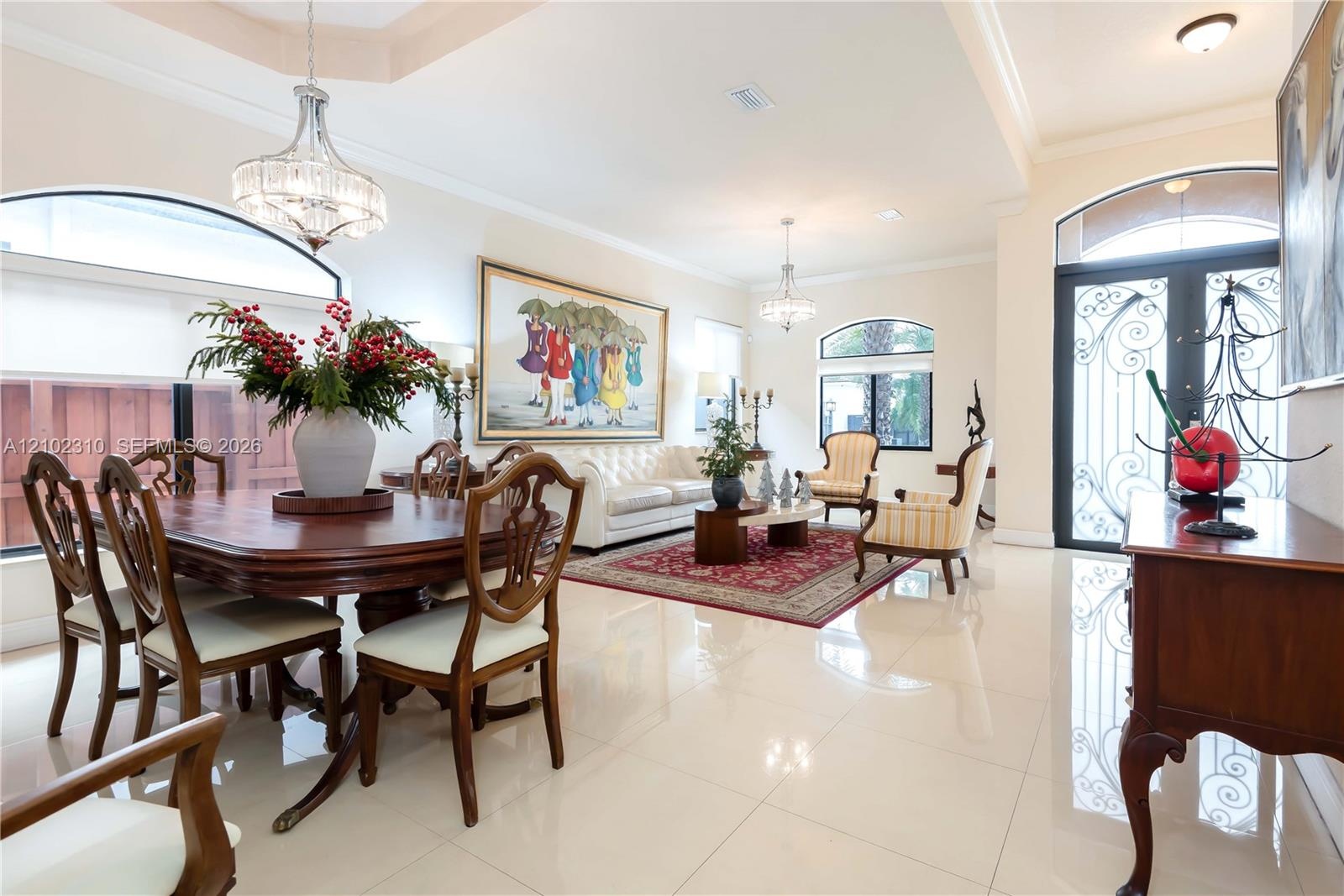 Open-concept living and dining area featuring polished tile flooring, tray ceilings, recessed lighting, decorative crystal chandeliers, and a wrought-