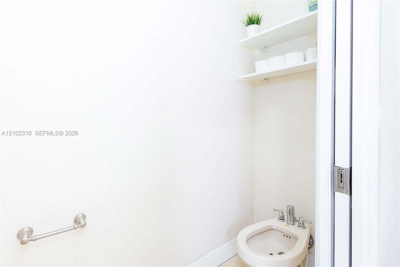Bidet with chrome fixtures, two wall-mounted shelves, and a wall-mounted metal towel bar