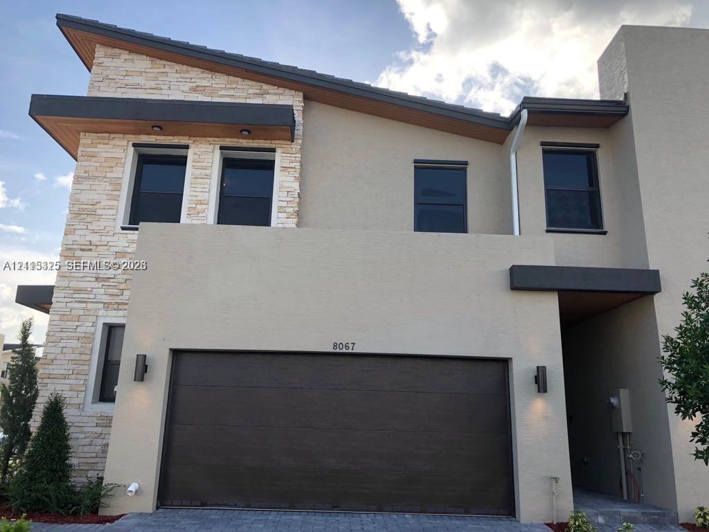 Contemporary two-story exterior featuring a stacked stone facade, shed roofline with wood-finish soffits, and a dark-toned paneled garage door