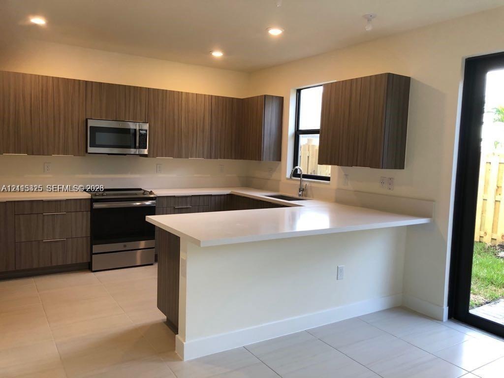 Kitchen featuring wood-finish cabinetry, stone-surface countertops, an integrated peninsula, stainless steel appliances, and tile flooring
