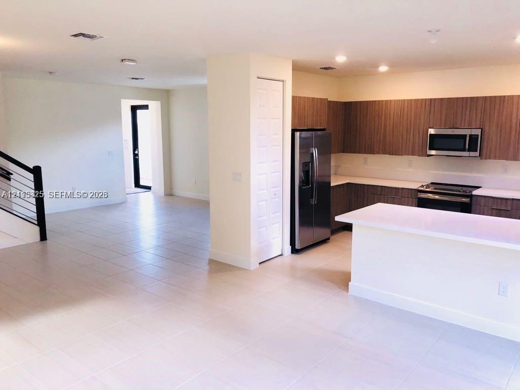 Kitchen featuring horizontal-grain cabinetry, quartz countertops, a stainless steel refrigerator, and a built-in microwave, accented by a staircase wi