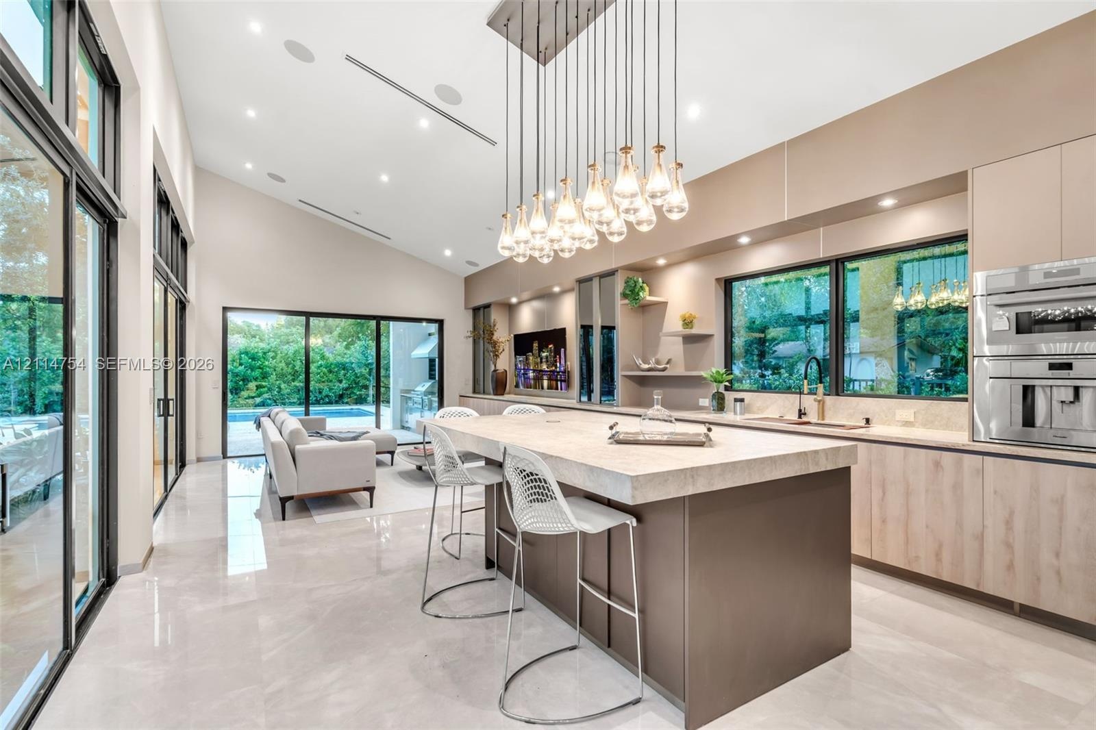 Chef’s kitchen featuring a large stone-topped island, floor-to-ceiling glass sliding doors, recessed lighting, multi-bulb pendant lighting, and built-