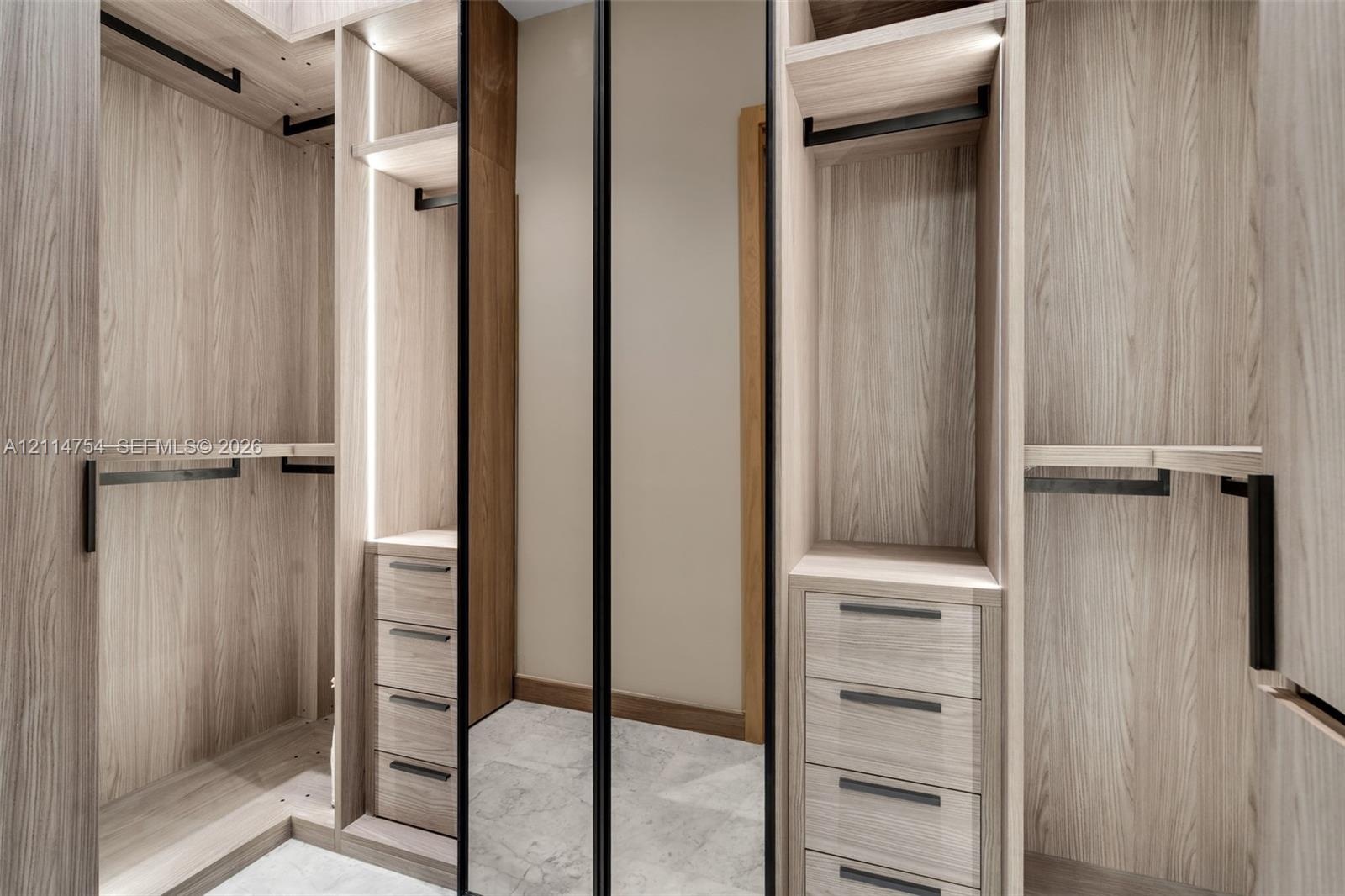 Custom walk-in closet featuring light wood-finish cabinetry, built-in drawer stacks with matte black pulls, vertical integrated LED accent lighting, f