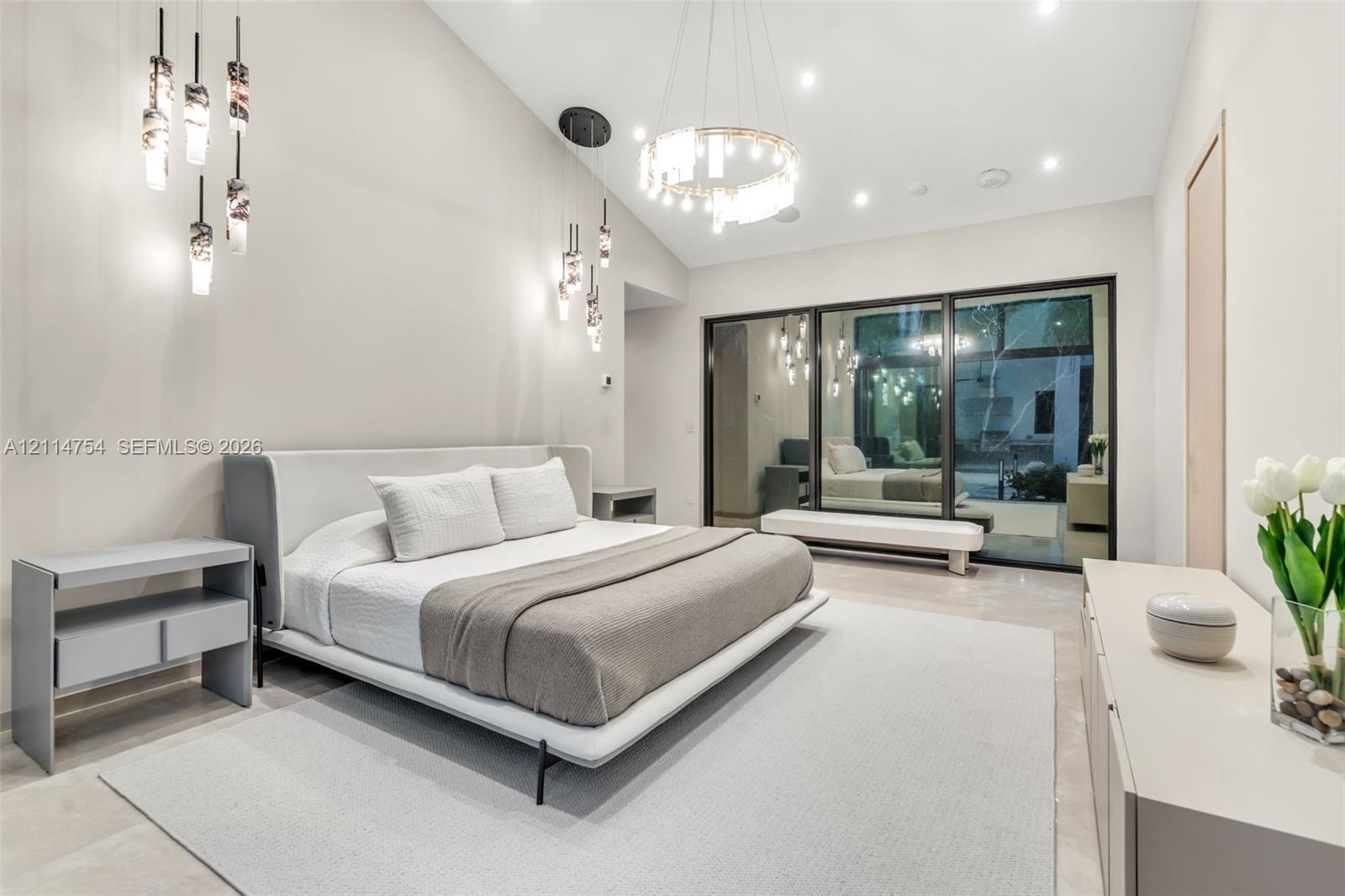 Vaulted ceilings featuring multi-tiered circular and drop-pendant lighting fixtures, floor-to-ceiling glass sliding doors, and light-toned hard-surfac