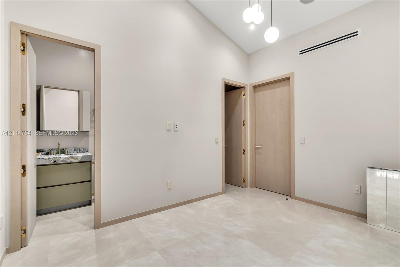 Vaulted ceilings featuring multi-pendant spherical lighting, light-toned wood-finish interior doors, and large-format neutral tile flooring