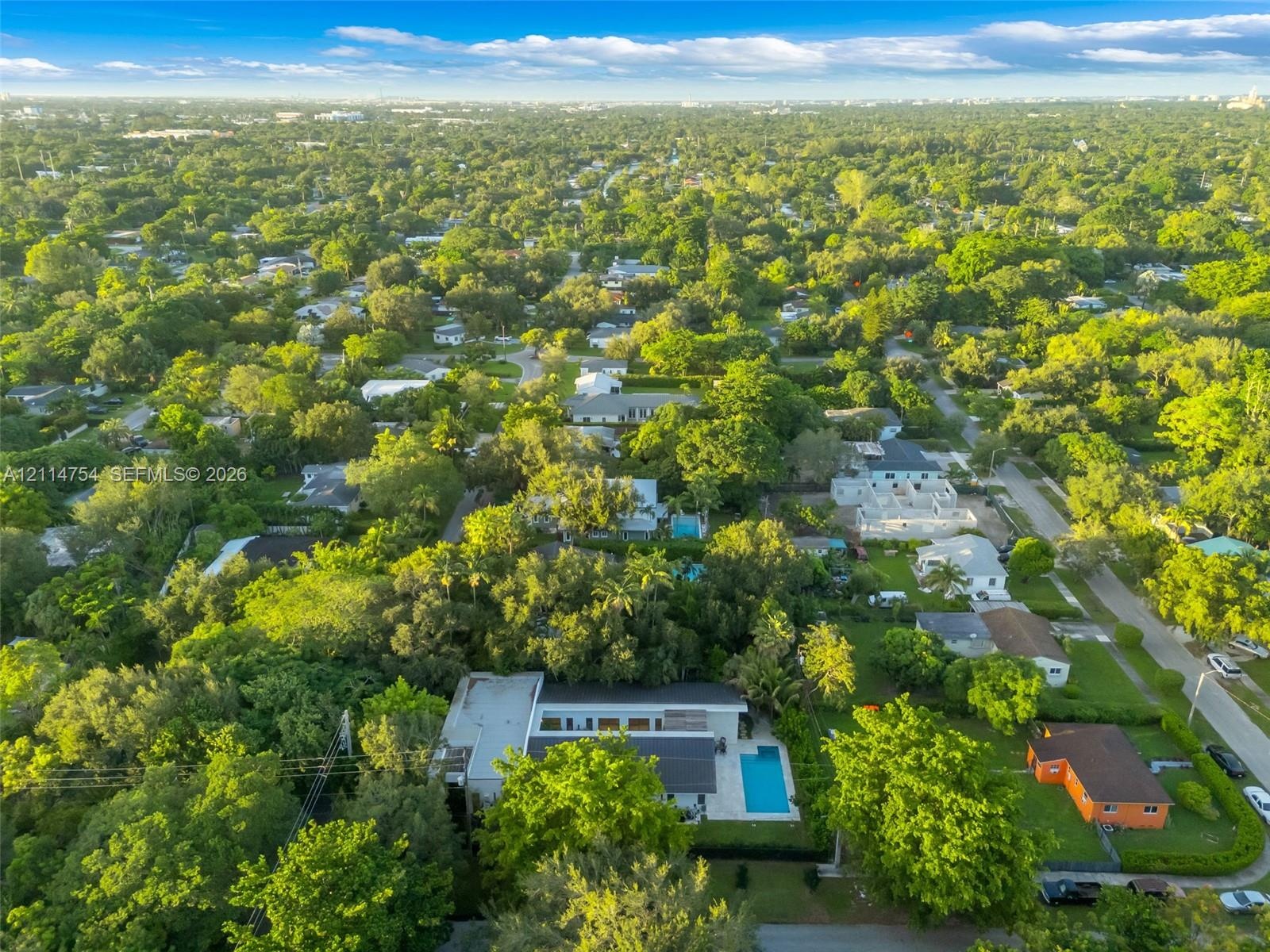 Aerial perspective of a contemporary residence featuring a flat roofline, a private rectangular pool, and extensive mature landscaping