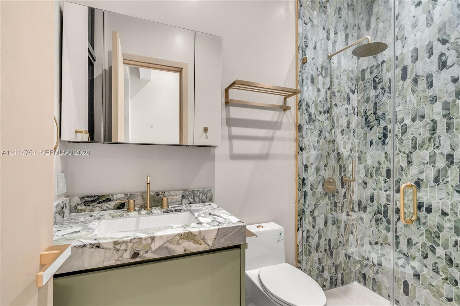 Modern vanity with a natural stone countertop and brass-finish faucet, featuring a mirrored medicine cabinet, a wall-mounted brass towel rack, and a g