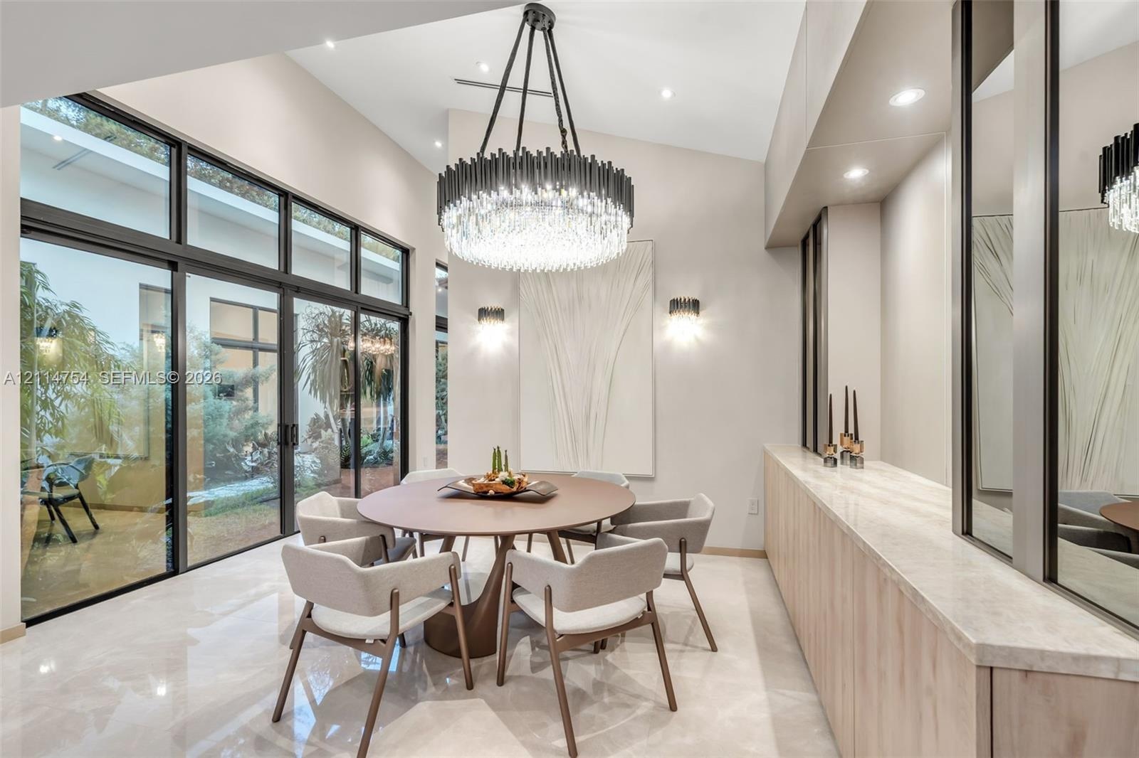 Vaulted ceilings with recessed lighting, full-height glass sliding doors, large-scale crystal and metal chandelier, built-in cabinetry with natural st