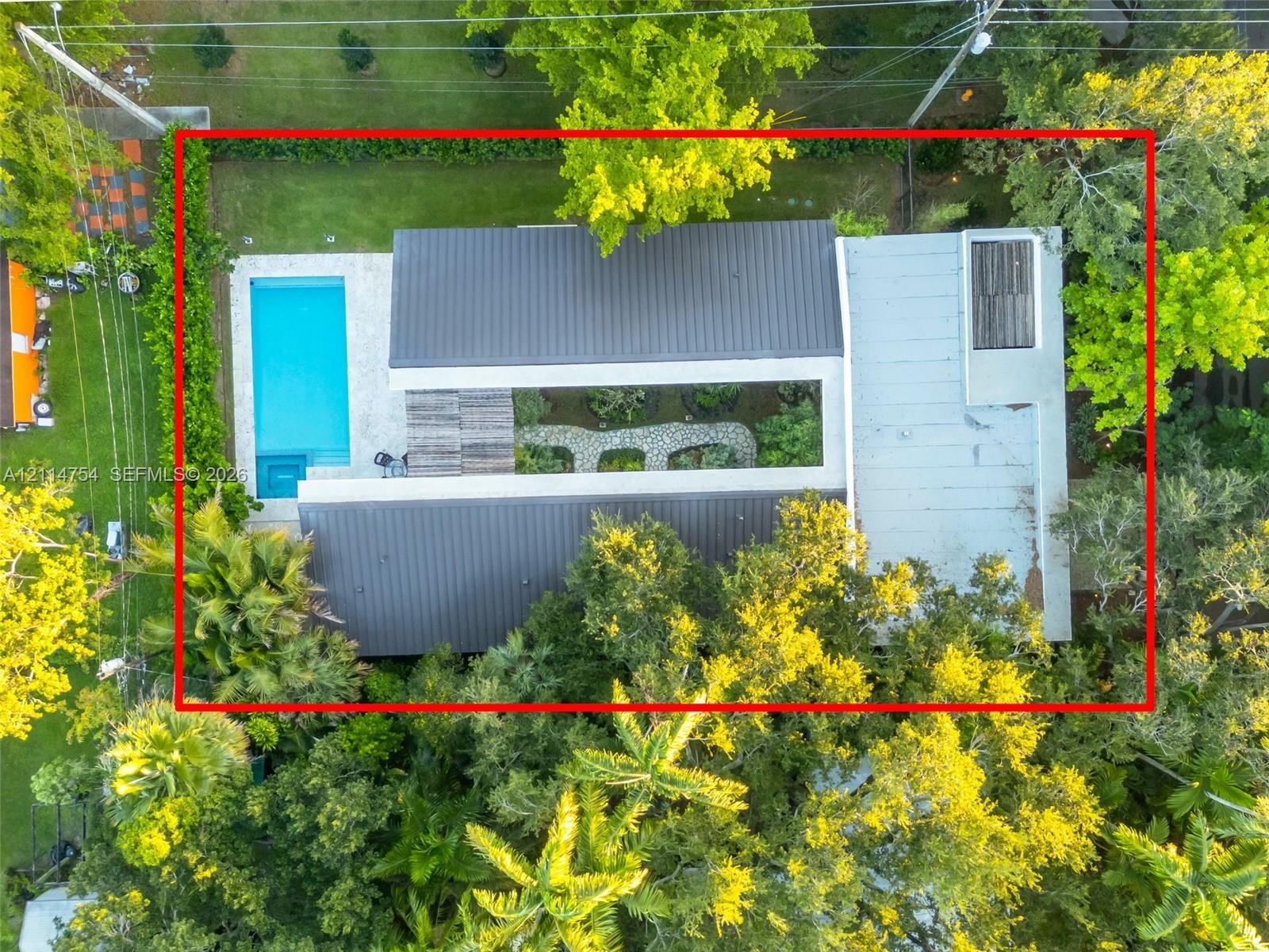 Aerial perspective featuring a rectangular swimming pool, central open-air courtyard with stone landscaping, multi-section metal roofing, and mature p