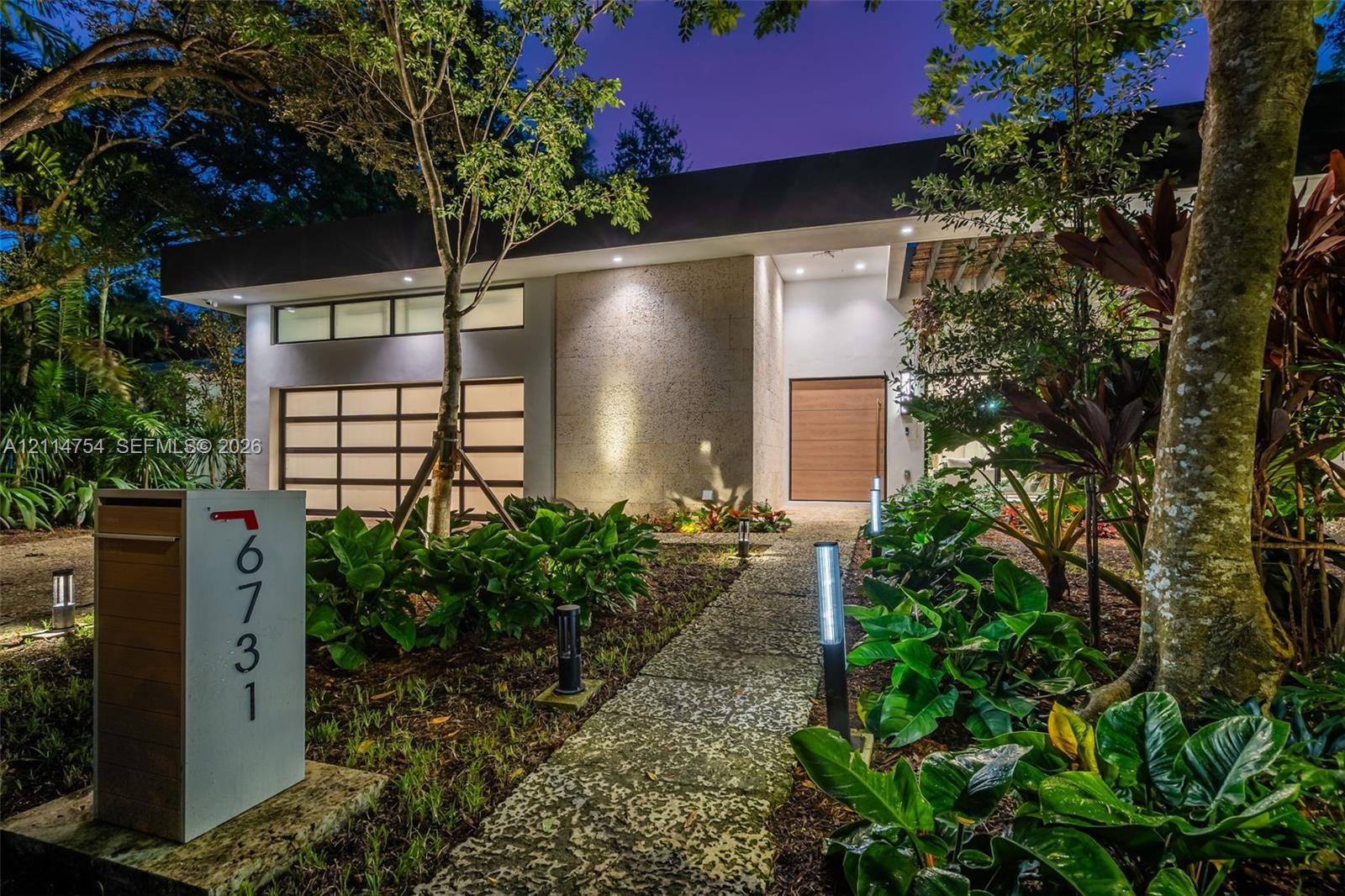 Modern exterior featuring a textured stone facade, multi-panel glass garage door, wood-finish entry door, and stone paver walkway