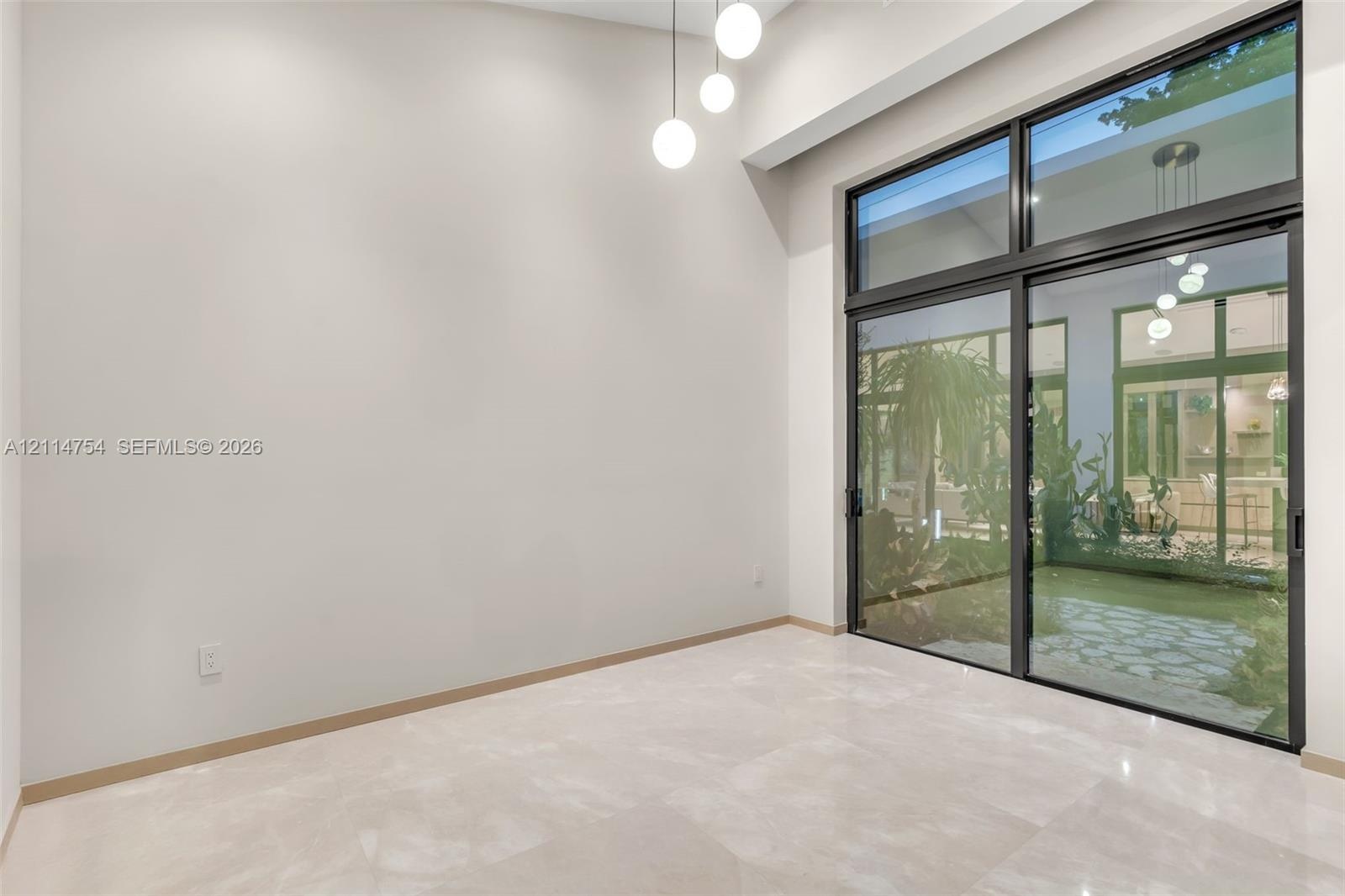 High ceilings featuring tiered globe pendant lighting, oversized sliding glass doors with dark frames, and polished neutral-toned tile flooring