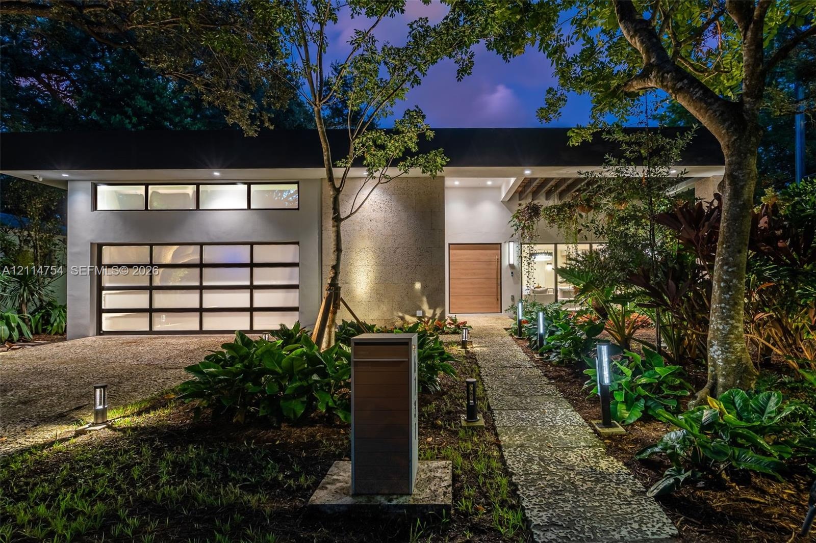Modern exterior featuring a flat roofline, clerestory windows, a multi-panel glass garage door, a natural wood entry door, and a stone-paver walkway
