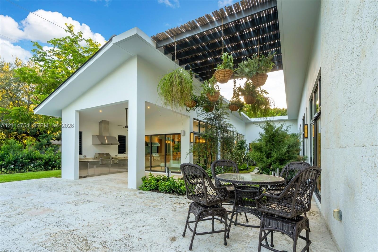 Covered patio featuring stone-tiled flooring, a built-in outdoor kitchen with stainless steel appliances, a slatted overhead architectural structure, 