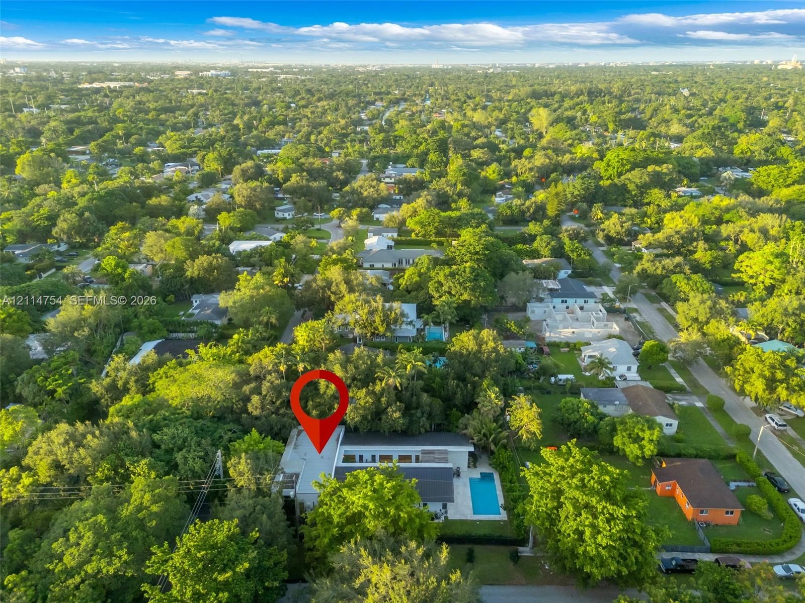 Aerial perspective of a property featuring a private swimming pool, flat roofline, paved patio, and dense mature perimeter landscaping