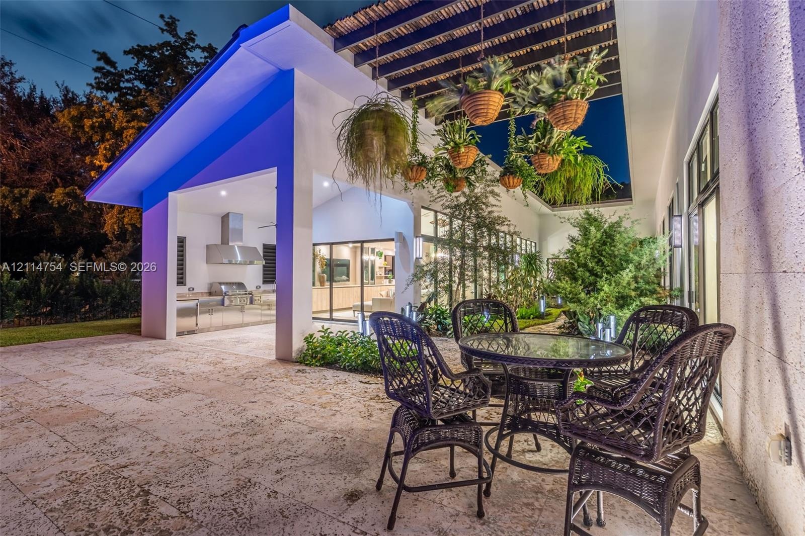 Covered outdoor patio featuring stone flooring, a slatted timber pergola, and a built-in outdoor kitchen with a stainless steel range hood
