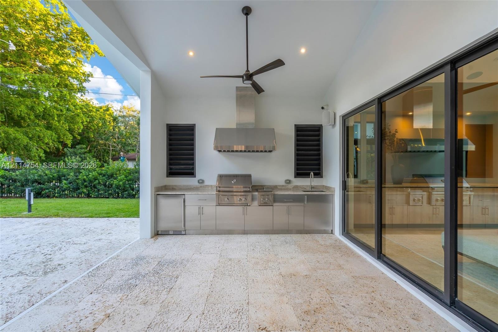 Covered patio featuring stone tile flooring, stainless steel outdoor kitchen with built-in grill, stone countertop, ceiling fan, and expansive sliding