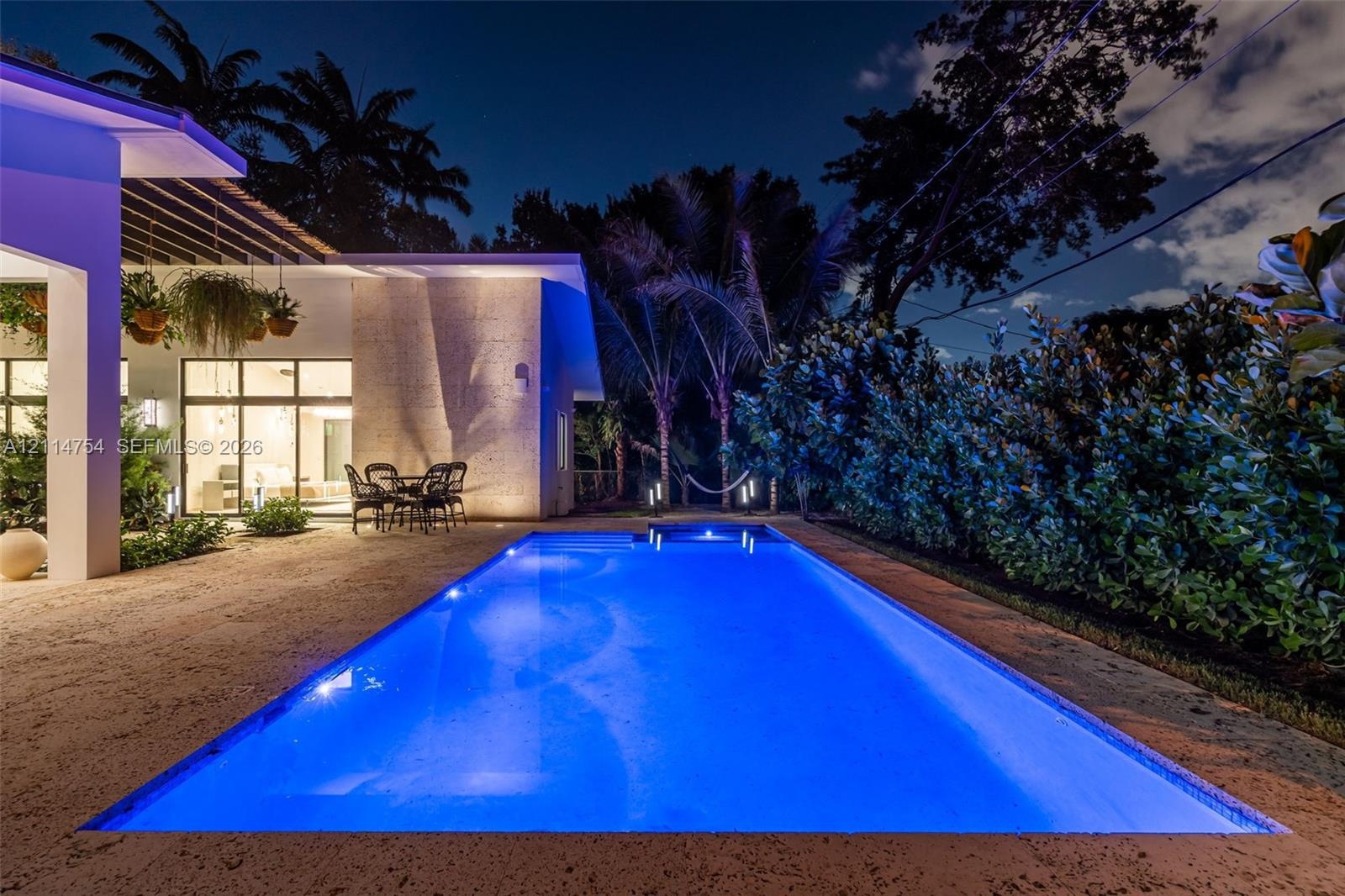 Rectangular in-ground pool with stone-finish decking, covered patio with structural pergola, and expansive glass sliding door panels