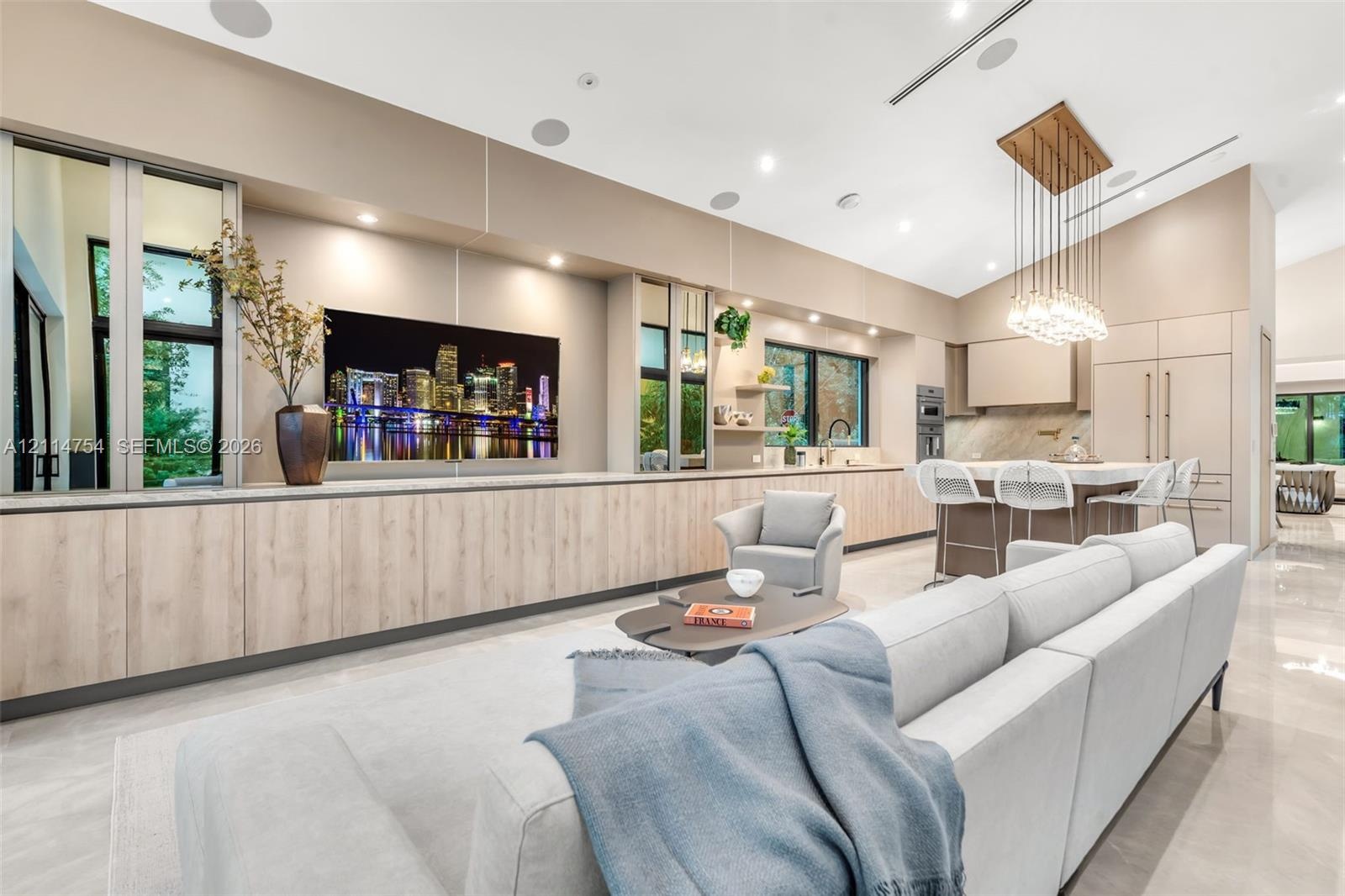 Vaulted ceilings, extensive custom cabinetry with light wood-finish detailing, recessed lighting, multi-light linear pendant fixture, and large-format