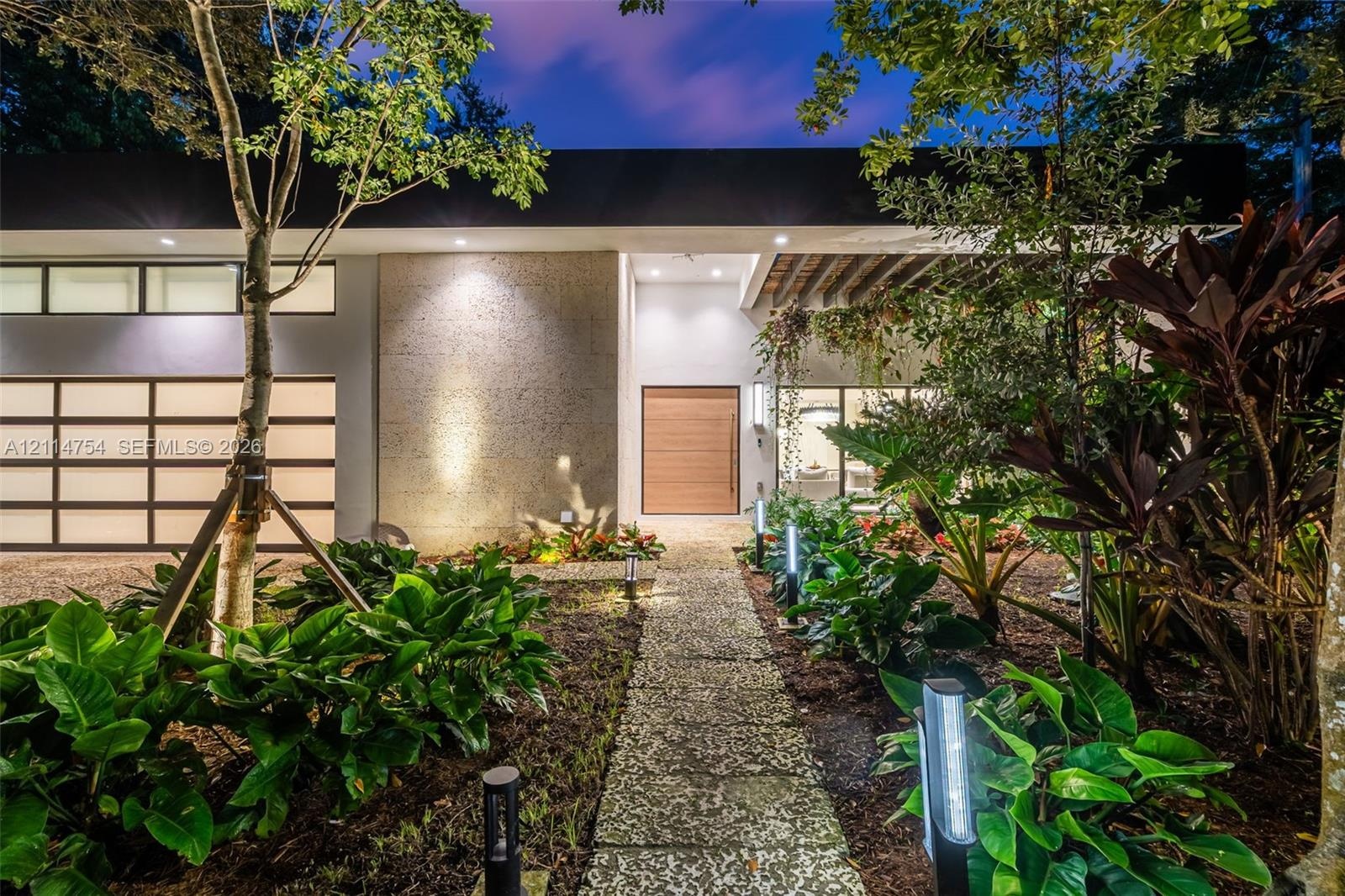 Modern contemporary facade featuring a textured stone accent wall, natural wood-finish front door, horizontal-pane garage door, overhead beam detailin