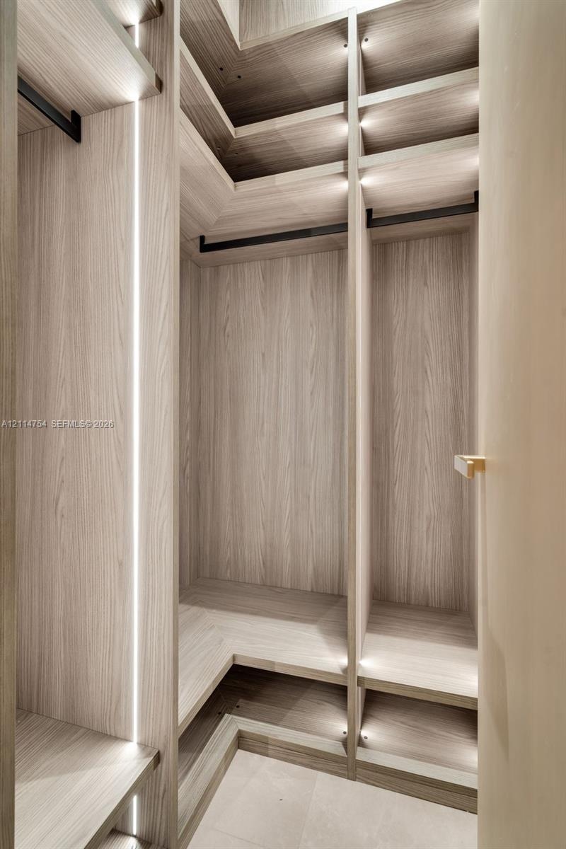 Custom wood-finish cabinetry featuring integrated vertical and recessed LED lighting, multi-level open shelving, and matte black hanging rods