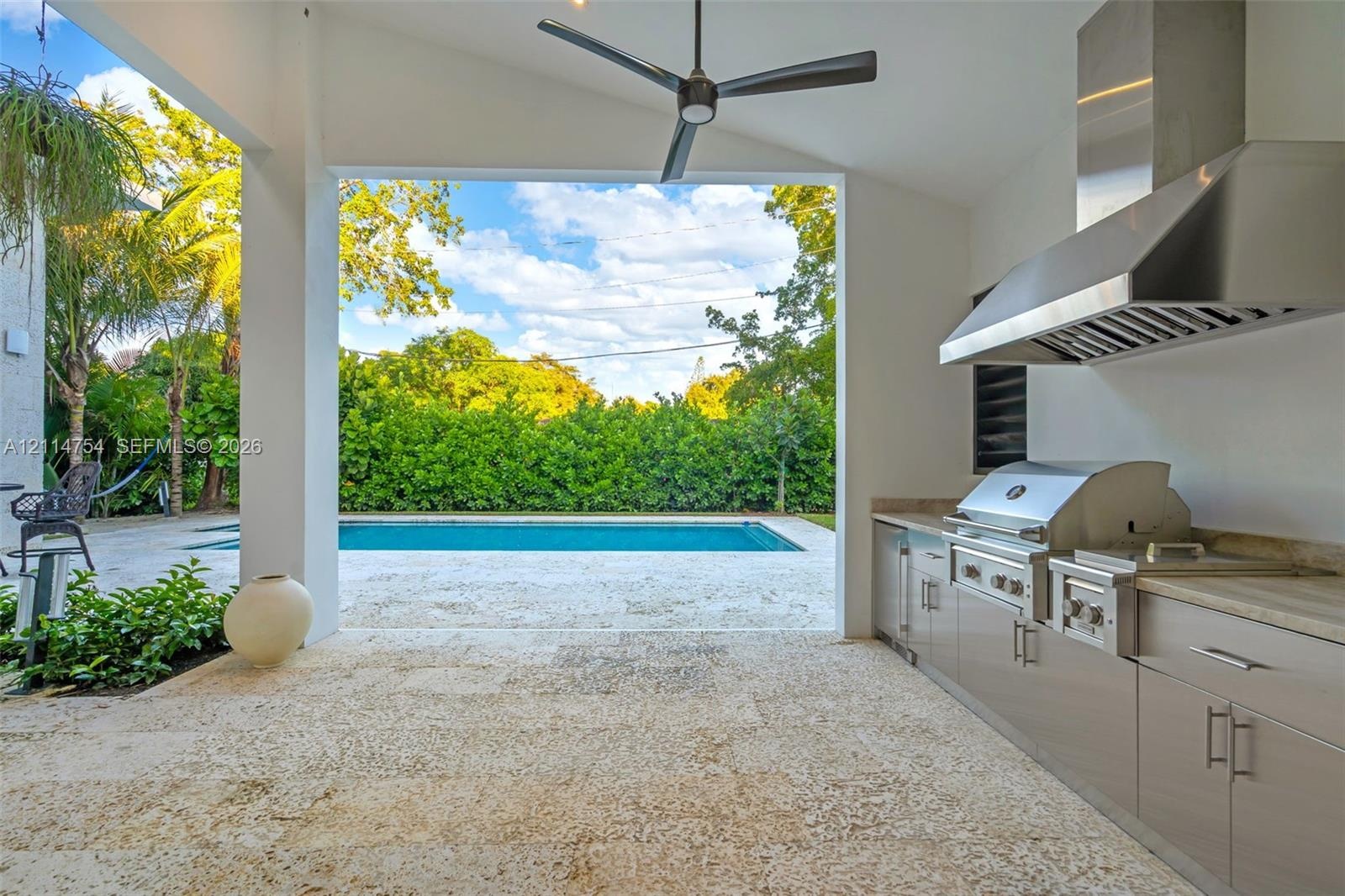 Covered outdoor kitchen featuring stainless steel cabinetry, a professional-grade grill, and a matching range hood, complete with natural stone floori