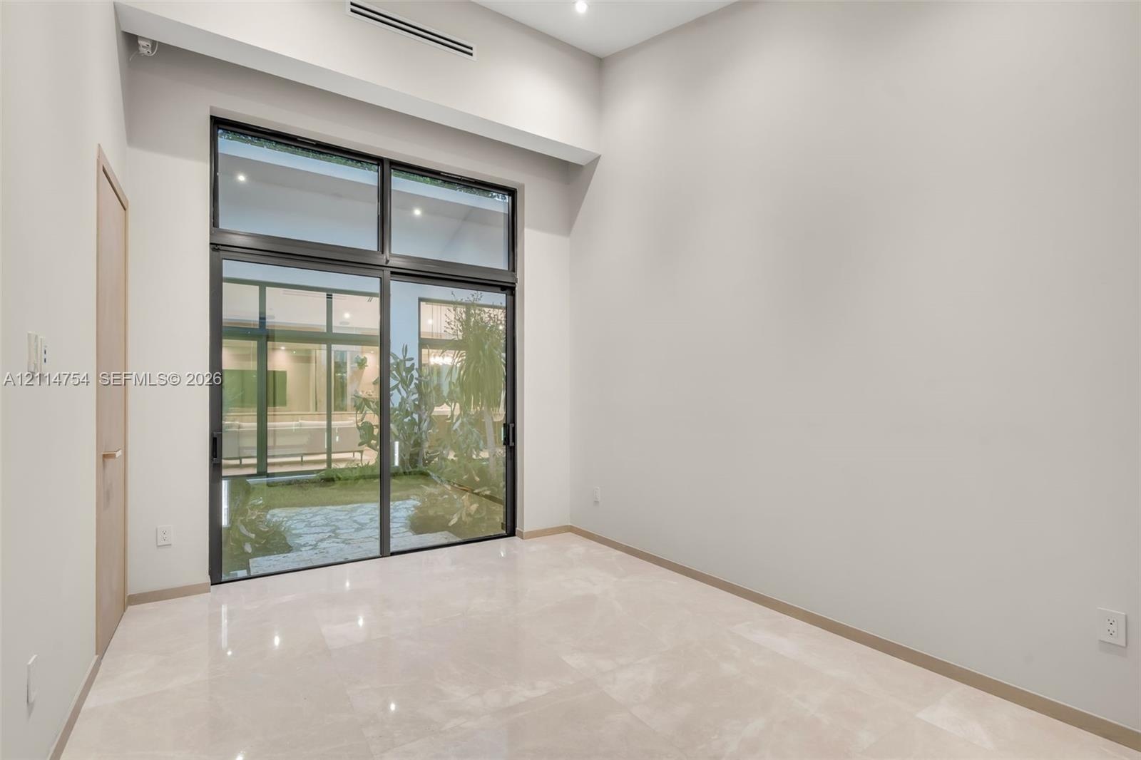 High-ceilinged room featuring large, floor-to-ceiling glass sliding doors, polished stone-finish flooring, recessed ceiling lighting, and a neutral co