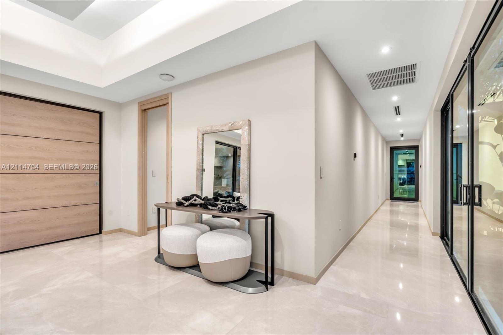 Foyer featuring large-format light-toned tile flooring, recessed ceiling lighting, a recessed tray ceiling, a large wood-finish door, and glass-panele