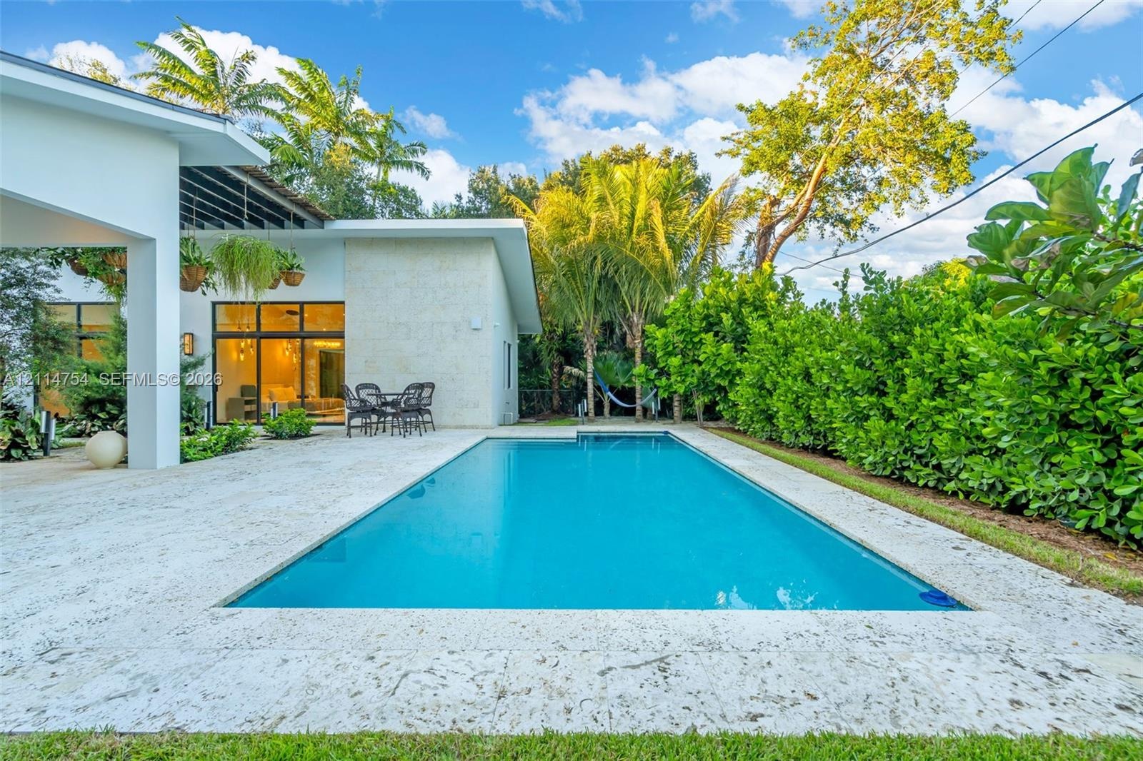 Rectangular swimming pool surrounded by stone-finish decking, covered patio space, and mature perimeter landscaping