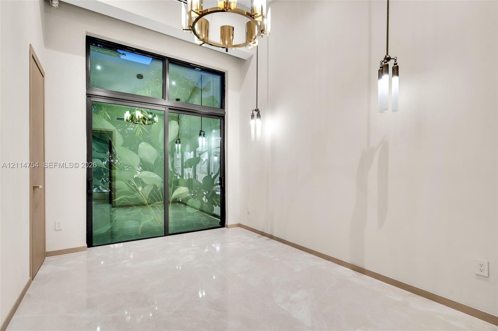 Interior space featuring high ceilings, polished stone-finish flooring, a multi-pane sliding glass door, a tiered metal chandelier, and a pendant ligh