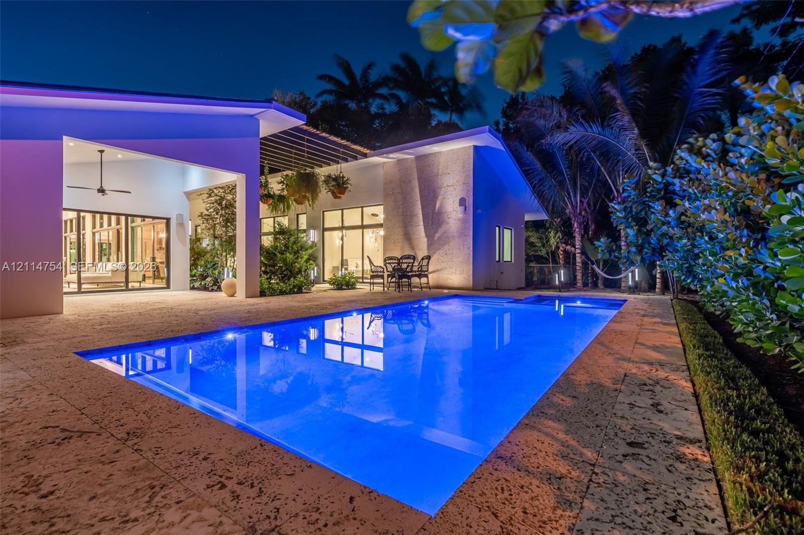 In-ground swimming pool with stone deck, covered patio, integrated pergola, and sliding glass wall systems