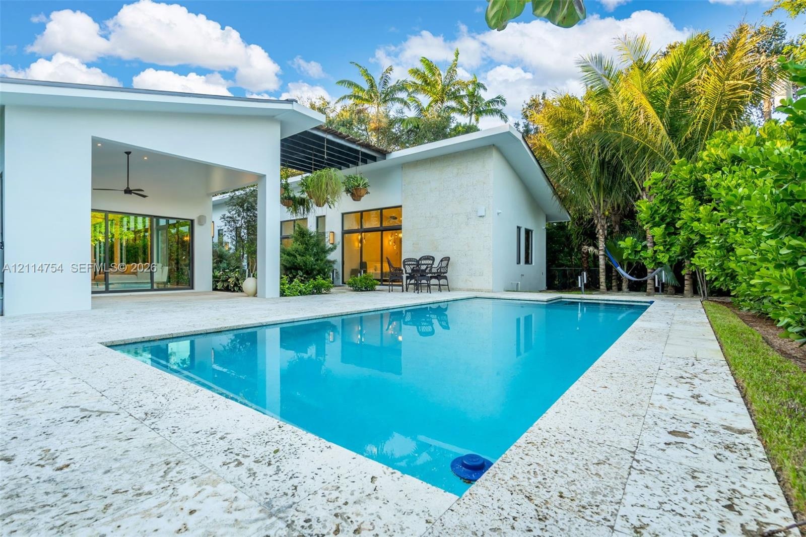 Swimming pool with stone-tiled decking, covered patio with integrated ceiling fan, and exterior wall cladding