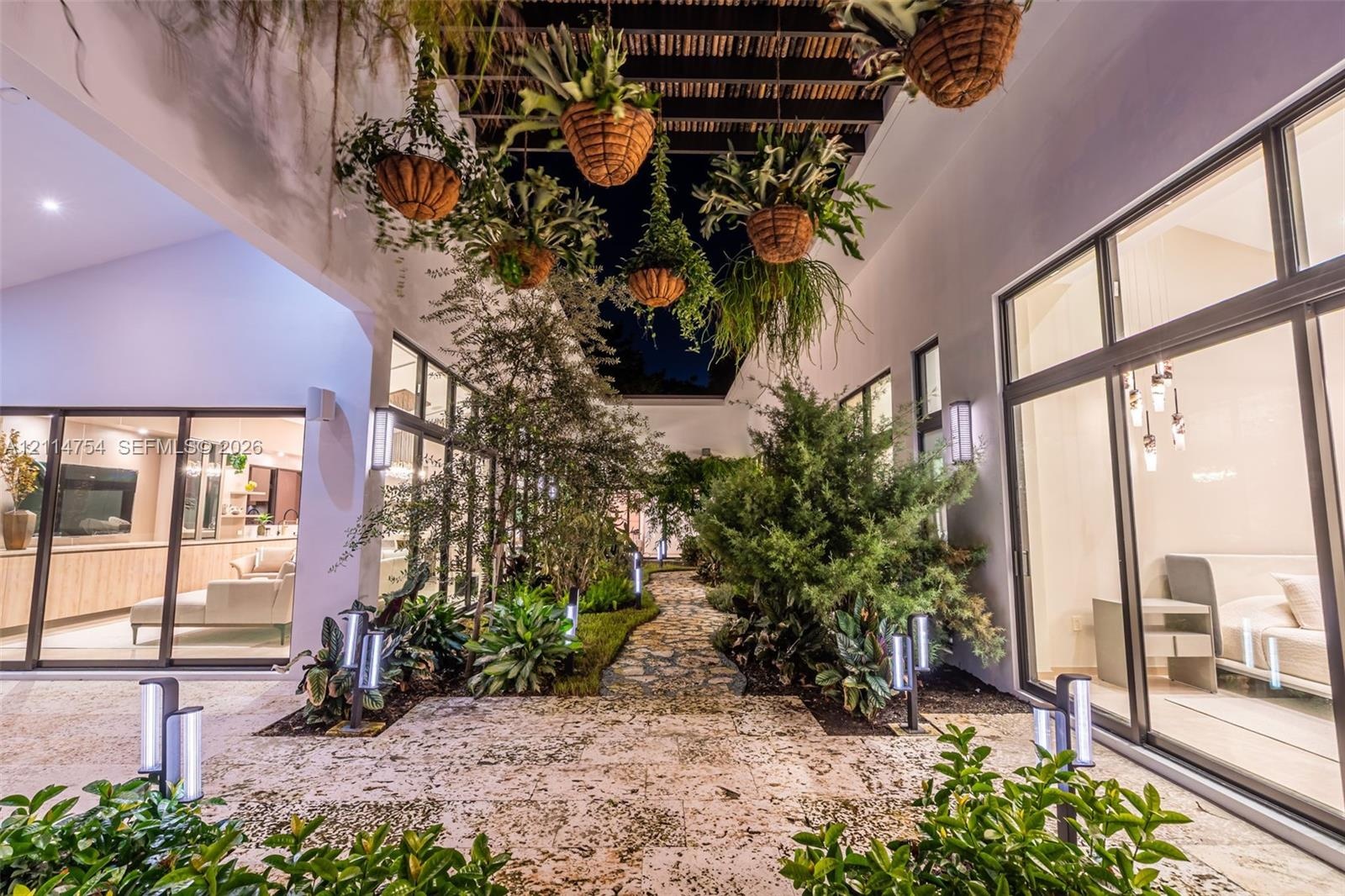 Enclosed courtyard featuring large-format stone pavers, a slatted timber pergola, floor-to-ceiling glass panel walls, and landscape lighting