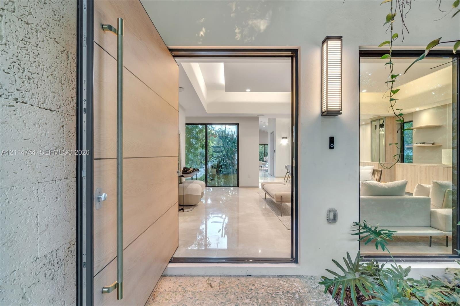 Pivot entry door featuring a light-toned wood finish and a long cylindrical metal handle, textured stone exterior wall, vertical wall-mounted exterior