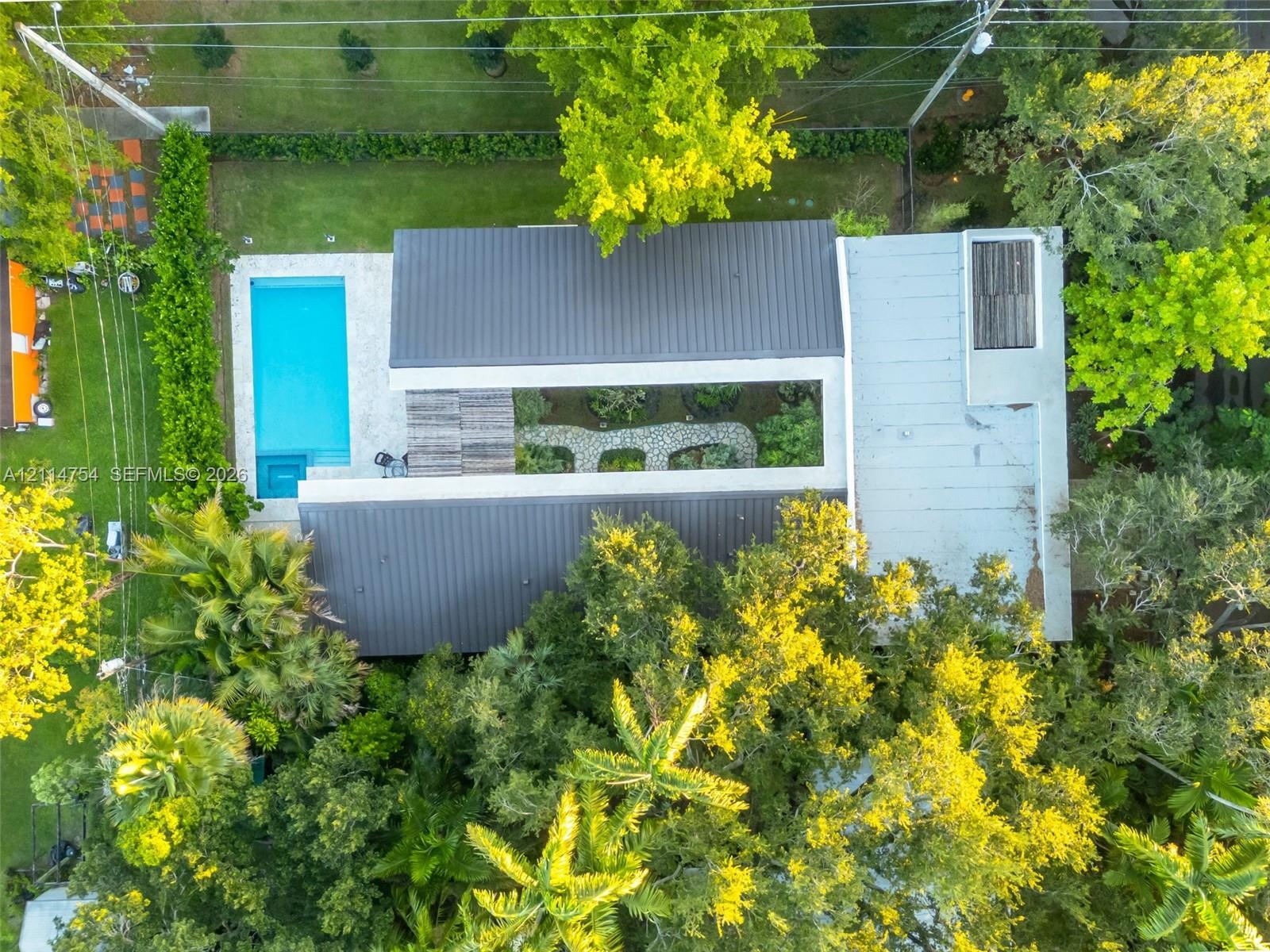 Aerial perspective featuring a rectangular swimming pool with hardscaped surround, integrated central garden courtyard, and standing seam metal roofin