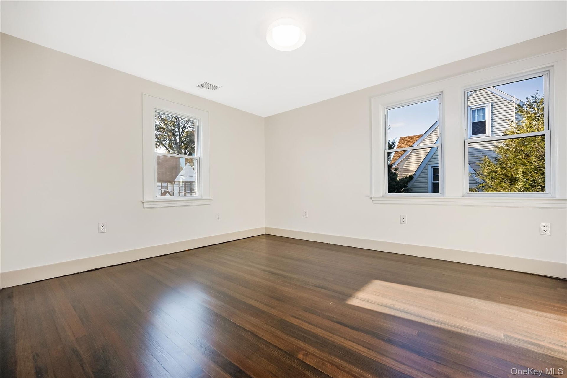 Bedroom featuring dark-stained wood-finish flooring, neutral wall paint, white trim, and multiple double-hung windows