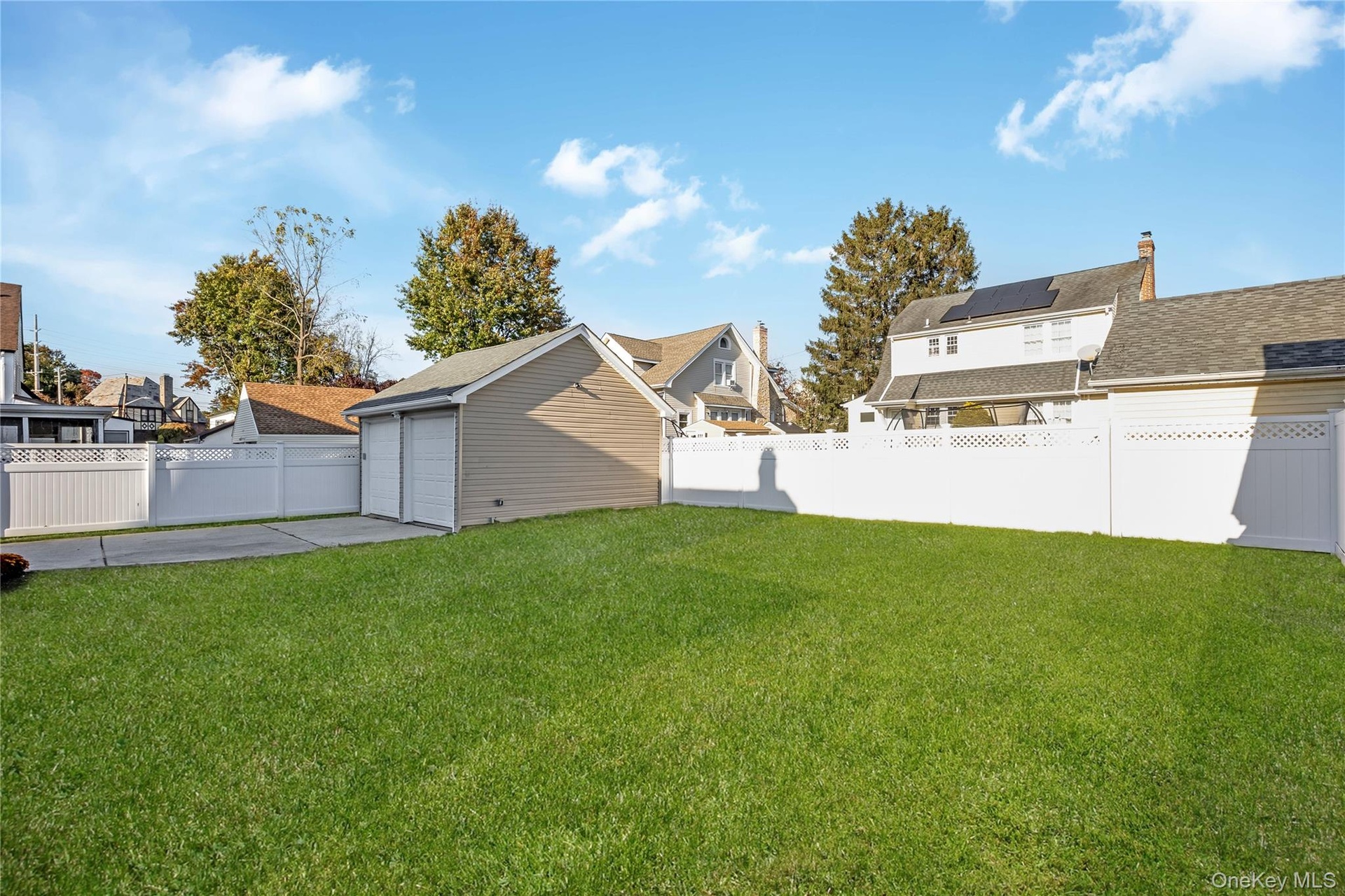 Backyard featuring a manicured lawn, detached two-car garage with electric and white vinyl privacy fencing. Grass is virtually enhanced