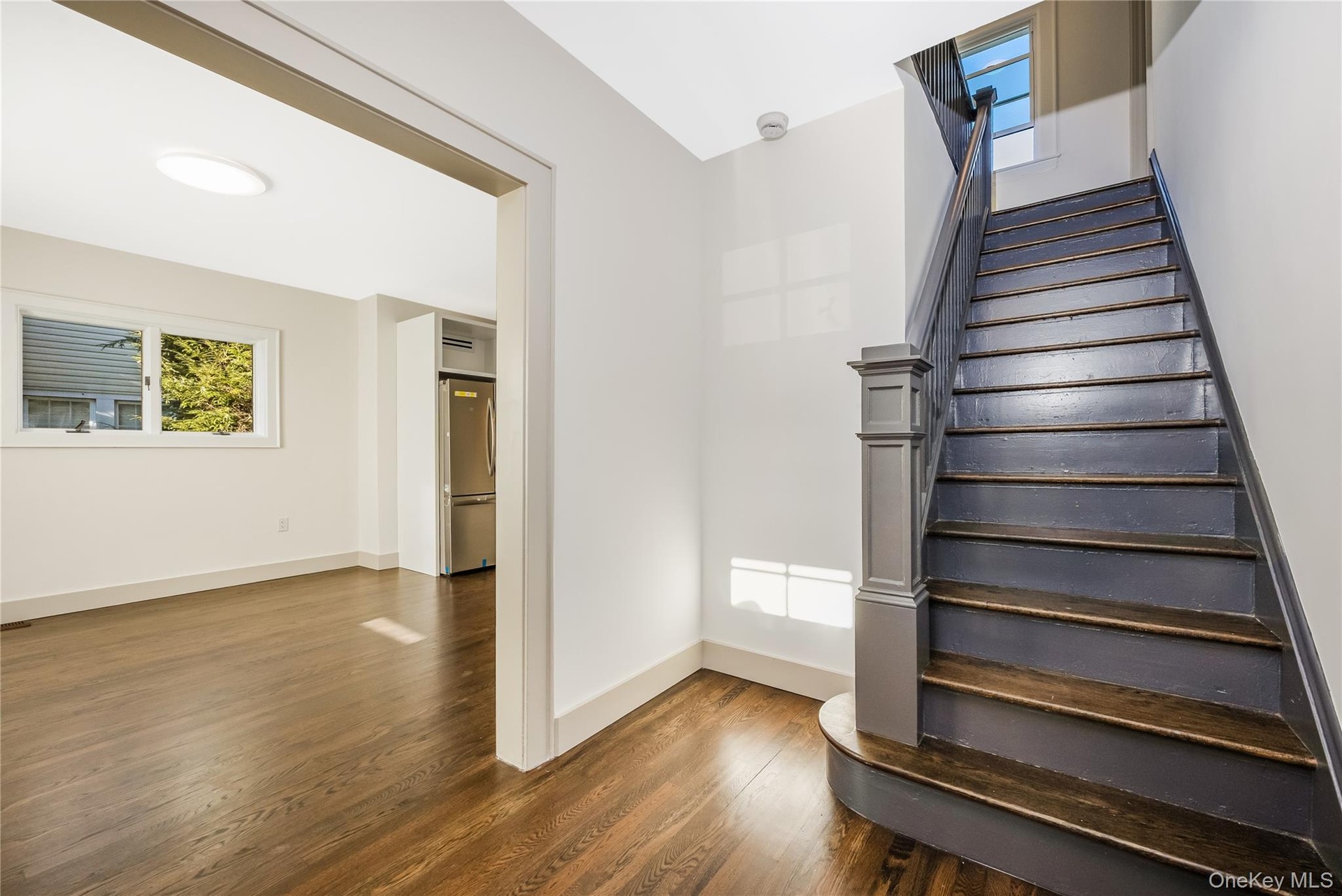 Staircase featuring a painted newel post, wood-finish flooring, and white walls