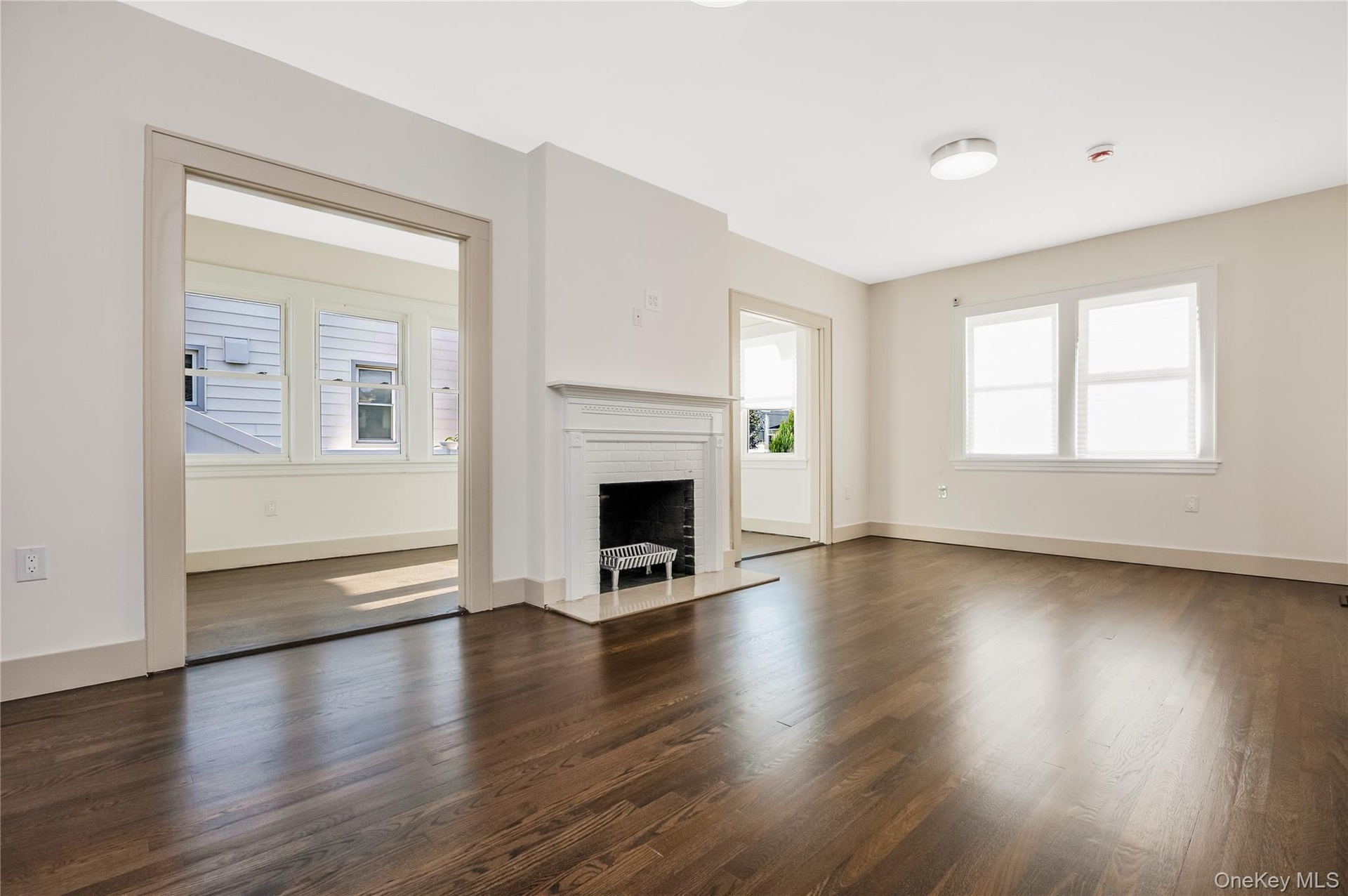 Living area featuring wood flooring, a traditional fireplace with a white mantel, and multi-pane windows