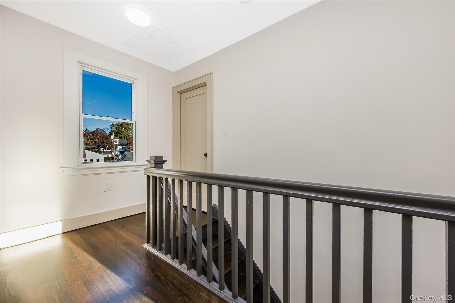 Dark wood-finish flooring, charcoal-painted spindle railing, neutral wall tones, and sash window