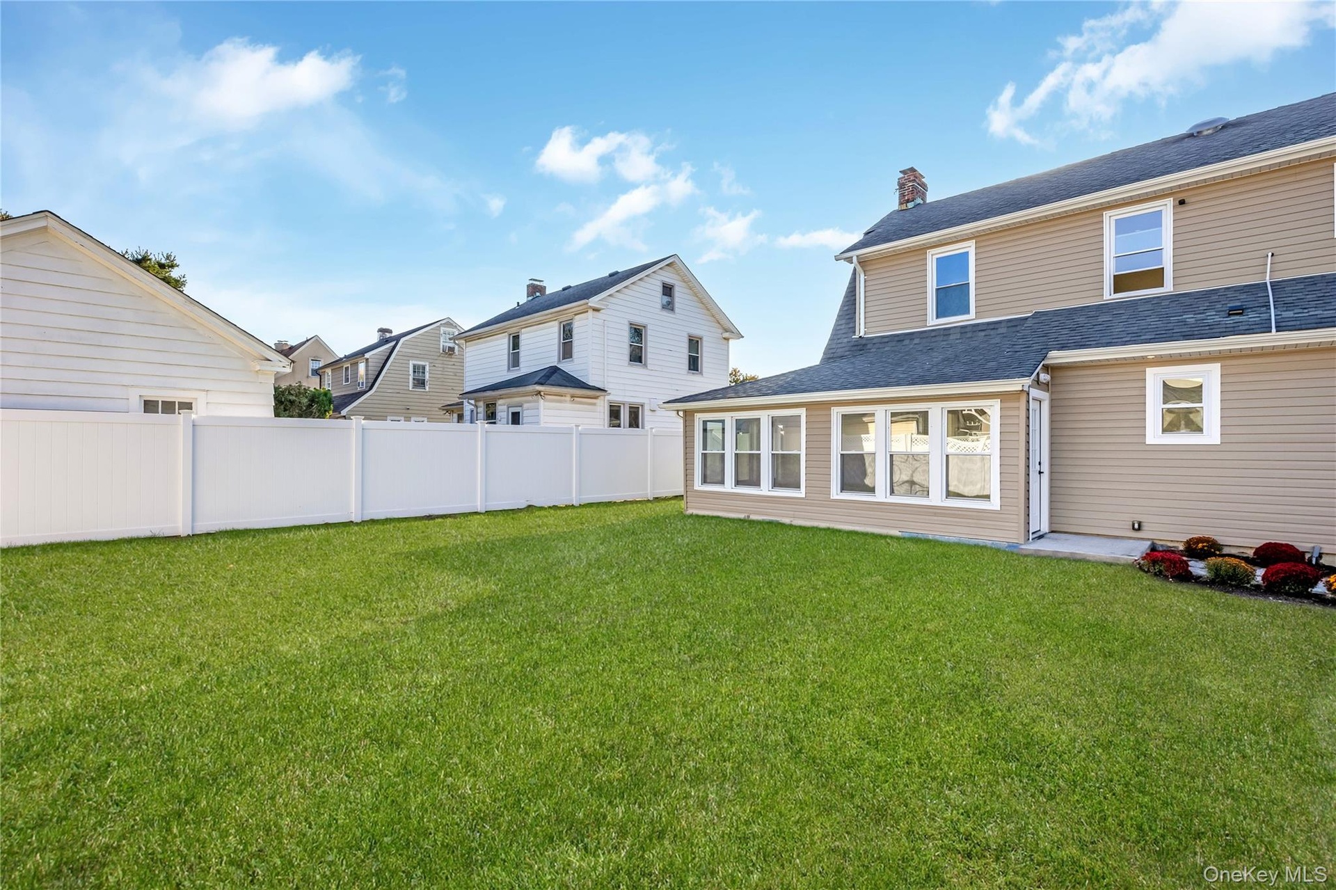 Backyard featuring a manicured lawn, full-perimeter vinyl privacy fencing, exterior siding, multi-pane windows, and a structured garden bed. Grass is 