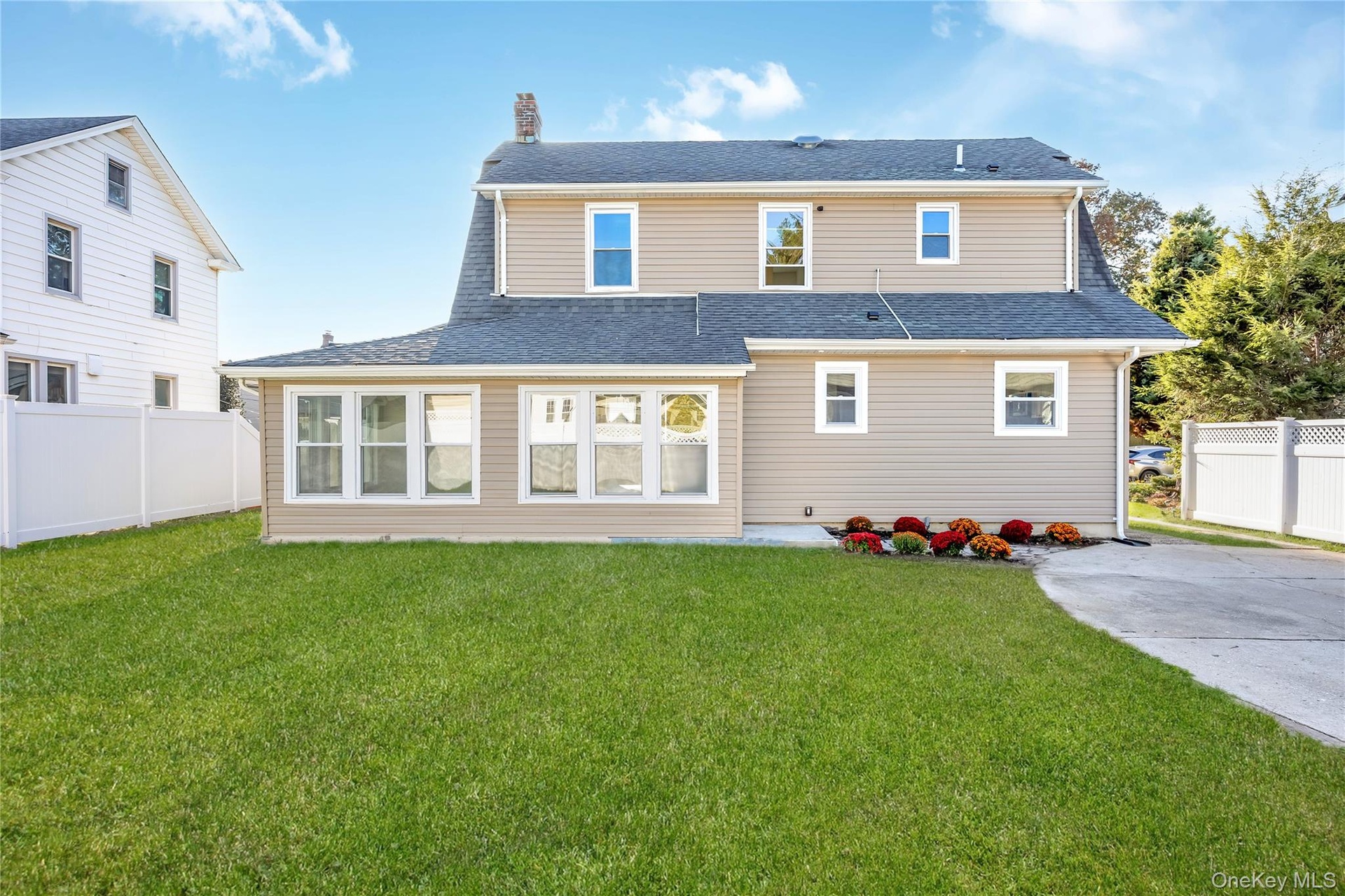 Back yard featuring light-toned horizontal siding, a multi-paneled window enclosed addition, an asphalt shingle roof, a concrete driveway, and a white
