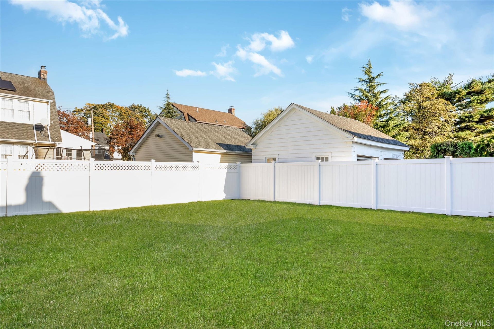 Expansive backyard featuring a level lawn and a full-height white vinyl privacy fence with lattice detailing. Grass is virtually enhanced